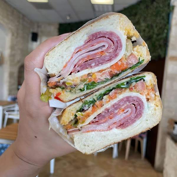 Hand holding a sliced Cuban sandwich with ham, salami, cheese, and vegetables.