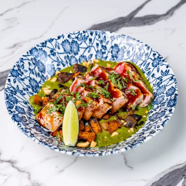 Seared tuna with green sauce, roasted vegetables, and a lime wedge in a blue and white patterned bowl.