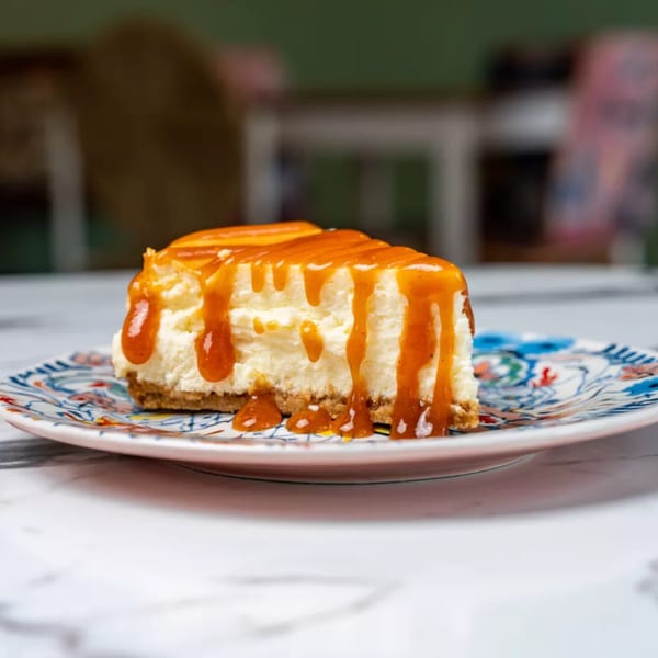 A slice of cheesecake with a graham cracker crust, drizzled with caramel sauce on a decorative plate.