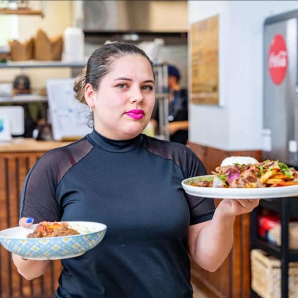 A Bilia Eatery staff member holds two plates of Cuban food, including a dish with rice and meat.