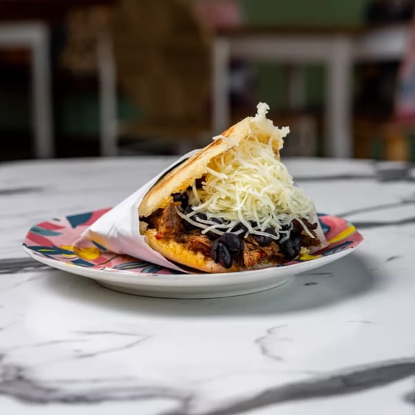 A Cuban arepa filled with shredded meat, black beans, and shredded cheese on a colorful plate.