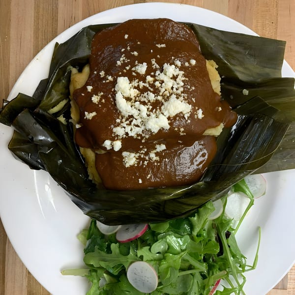 Cuban tamale with dark sauce and crumbled cheese, served with a side salad on a white plate.