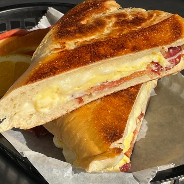 Close-up of a Cuban sandwich cut in half, revealing scrambled eggs, cheese, and ham.