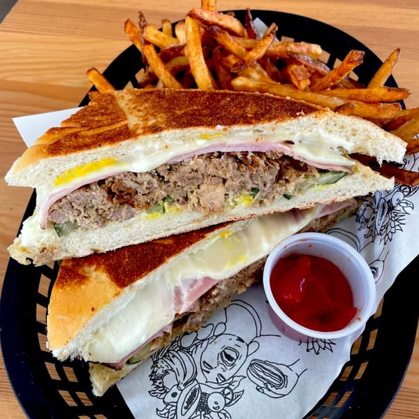 A Cuban sandwich with fries and ketchup in a black basket on a wooden table.