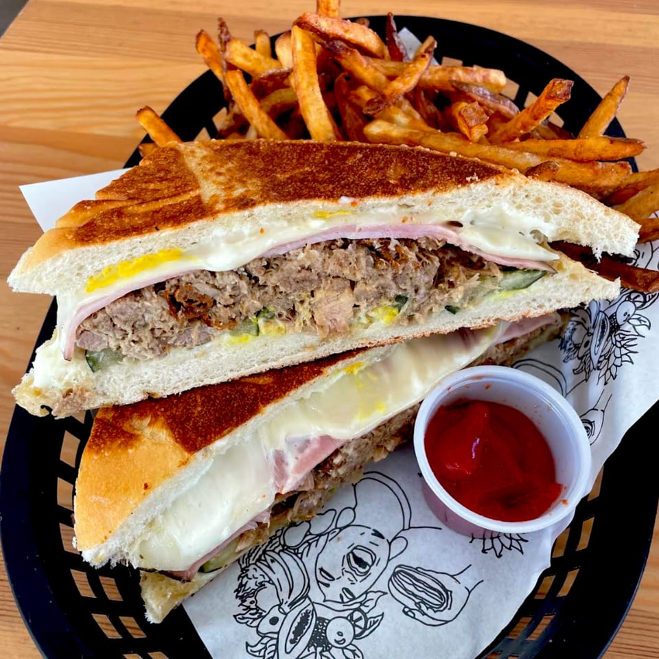 A Cuban sandwich with fries and ketchup in a black basket on a wooden table.