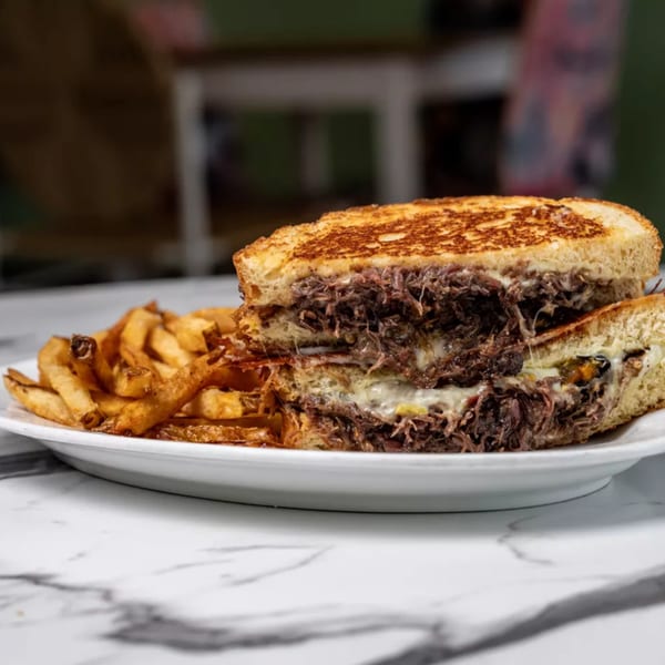 Close-up of a Cuban sandwich with shredded beef and melted cheese, served with golden fries.