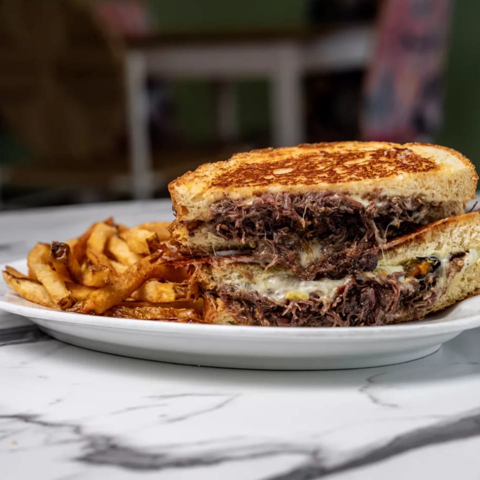 Close-up of a Cuban sandwich with shredded beef and melted cheese, served with golden fries.