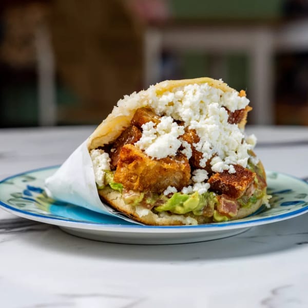 A Bilia Eatery arepa filled with fried pork, avocado, and crumbled white cheese on a plate.