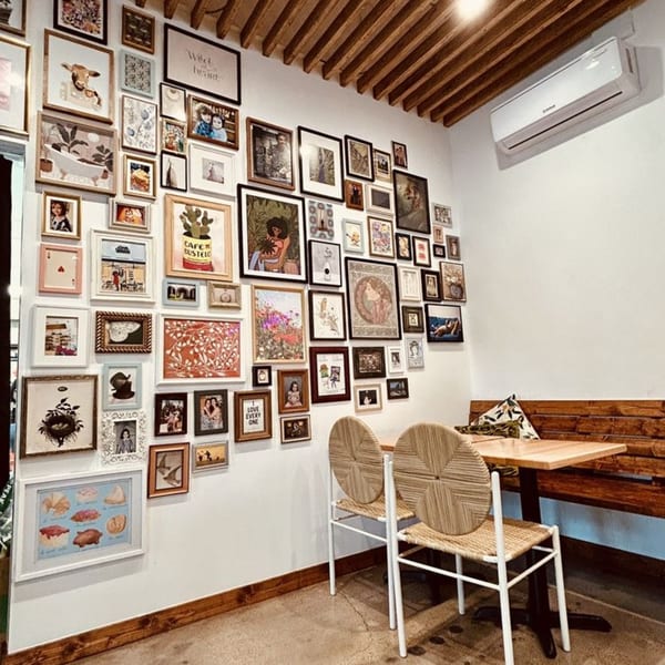 A cozy corner of Bilia Eatery with a gallery wall of framed art and a wooden bench with tables.