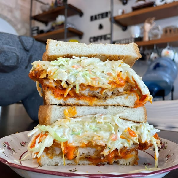 A towering fried chicken sandwich with coleslaw and orange sauce on white bread from Bilia Eatery.