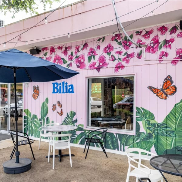 Bilia Eatery's pink exterior with vibrant murals of flowers, butterflies, and tropical leaves, featuring outdoor seating.