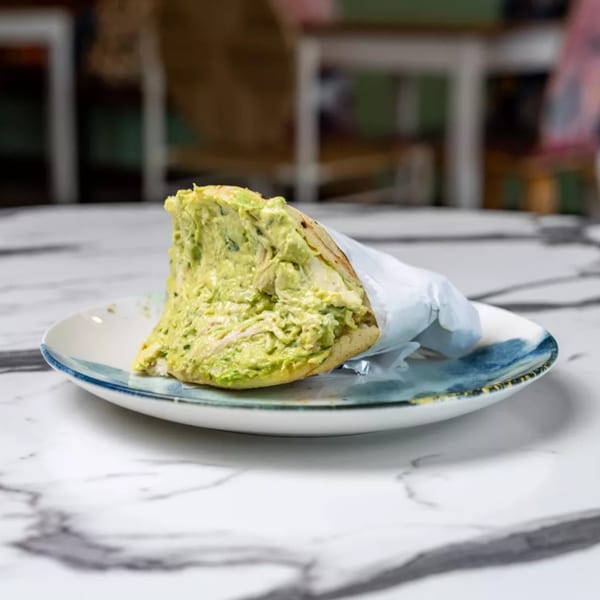 A Bilia Eatery Cuban arepa, generously filled with creamy avocado and chicken salad, on a marble table.