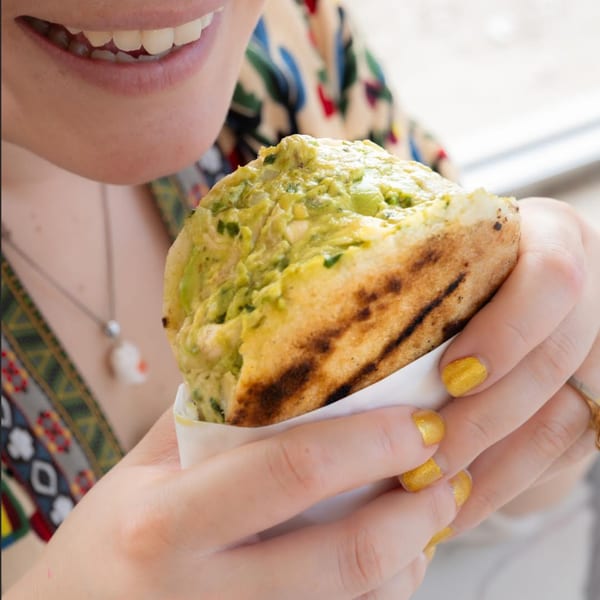 A person with yellow nail polish holds a Cuban arepa filled with green avocado salad.